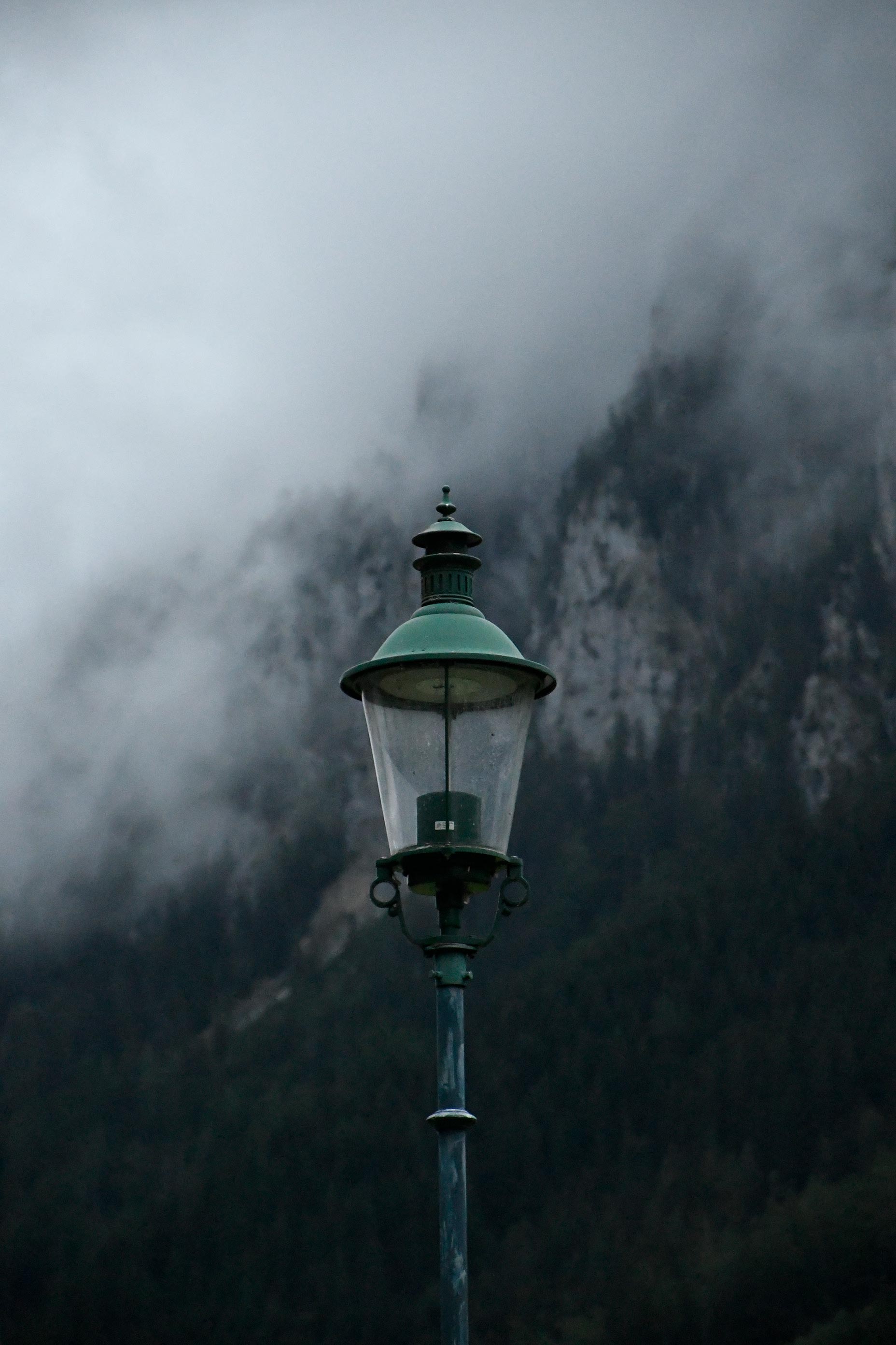 Ein Bild einer ausgeschalteten Straßenlaterne. Im Hintergrund sieht man vernebelte Bergfelsen.