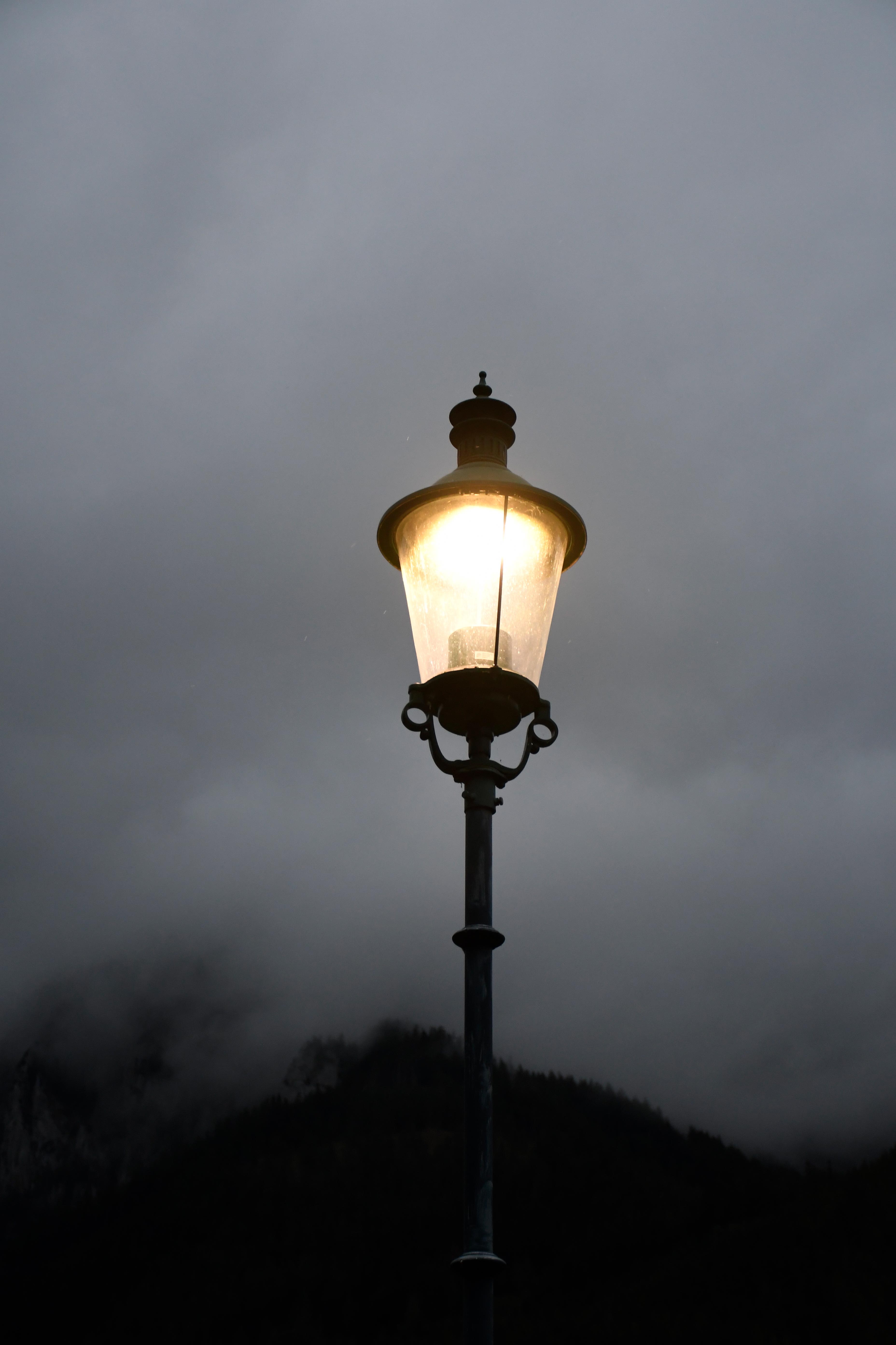 Ein Bild einer angeschaltenen Straßenlaterne. Im Hintergrund sieht man vernebelte Bergfelsen.